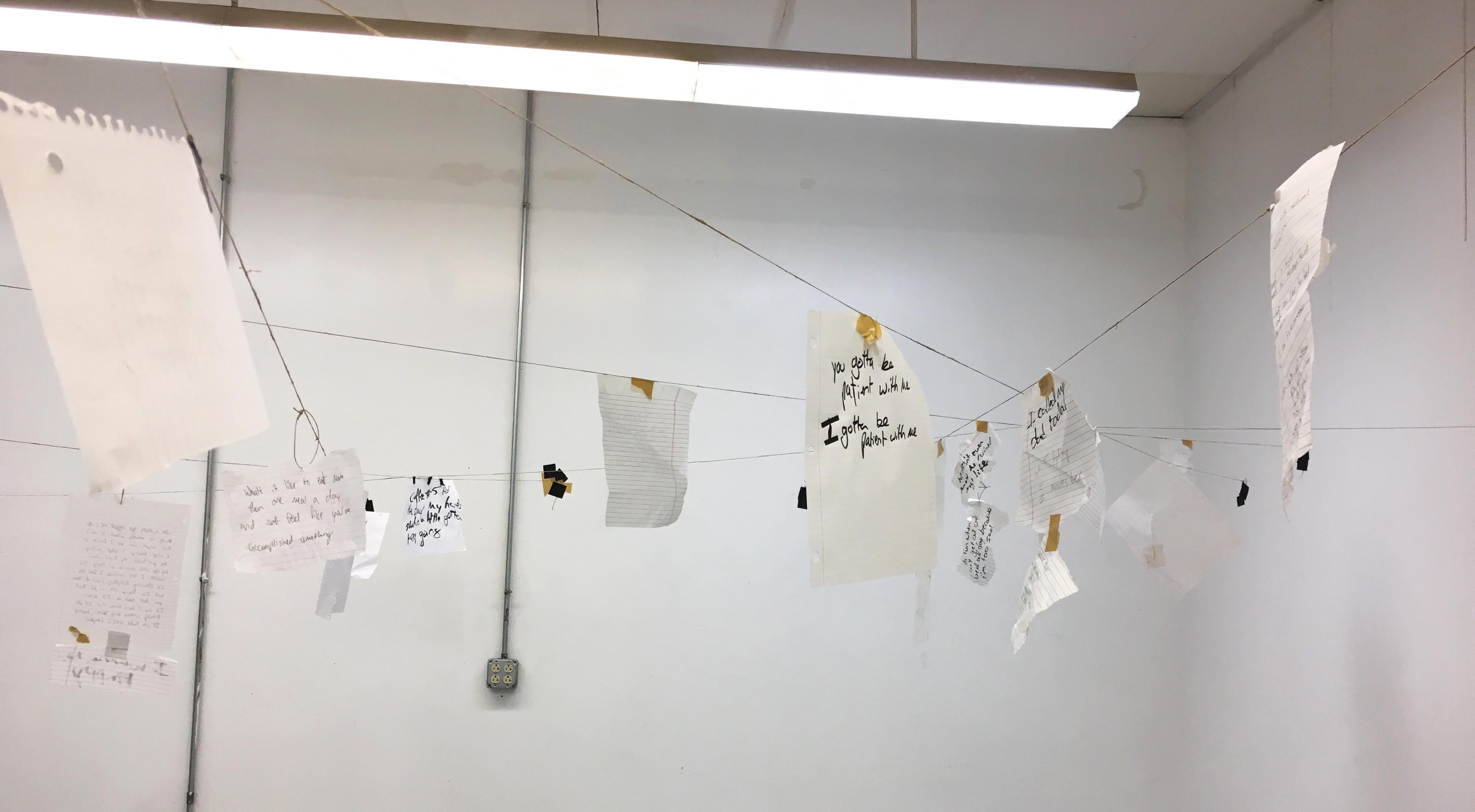 perspective of various pieces of paper with writing hung on hemp lines across a room