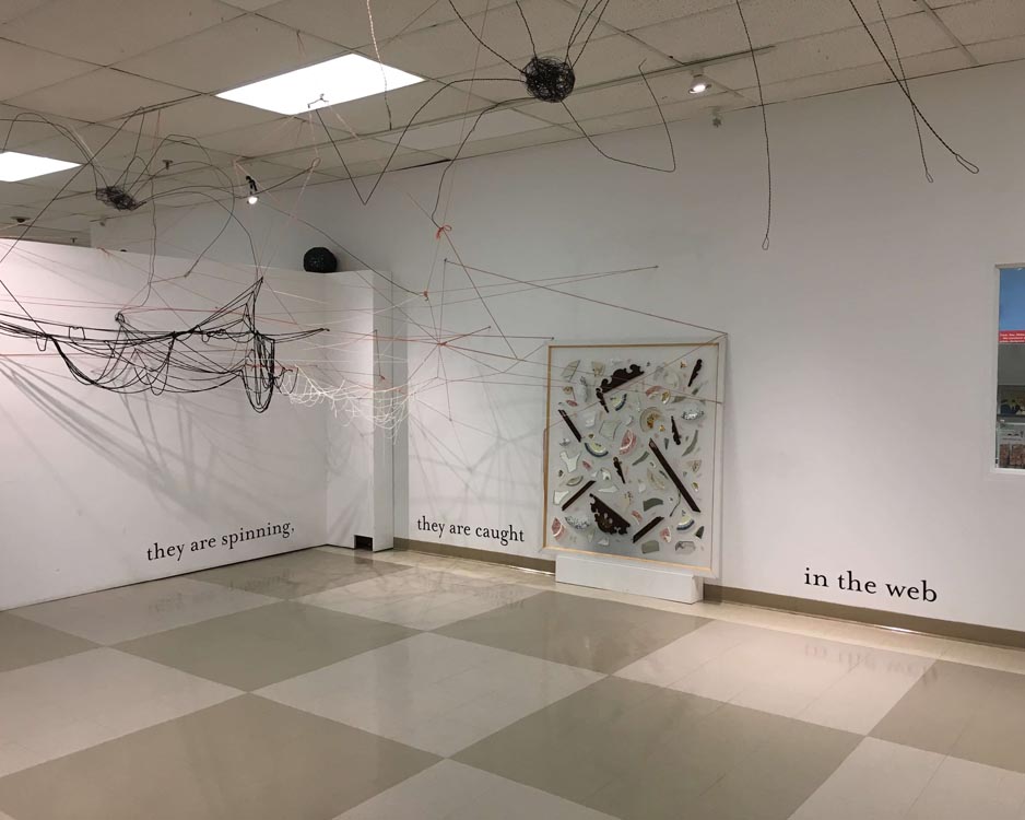 shot of gallery instal showing large vinyl text, a yarn spiderweb, and a large canvas sculpture