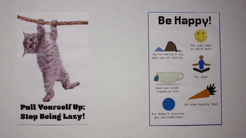 two posters one reading 'pull yourself up; stop being lazy' with a cat hanging on a rope and the other reading 'be happy' with unhelpful suggestions like 'have you tried chamomile tea?'